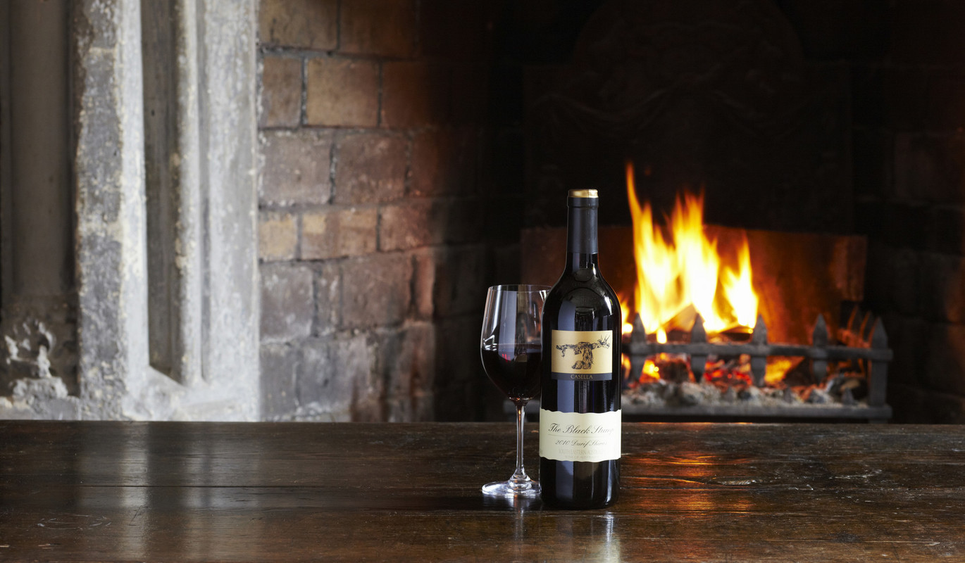 Our No.1 best-selling red The Black Stump Durif Shiraz with a glass in front of an open fire