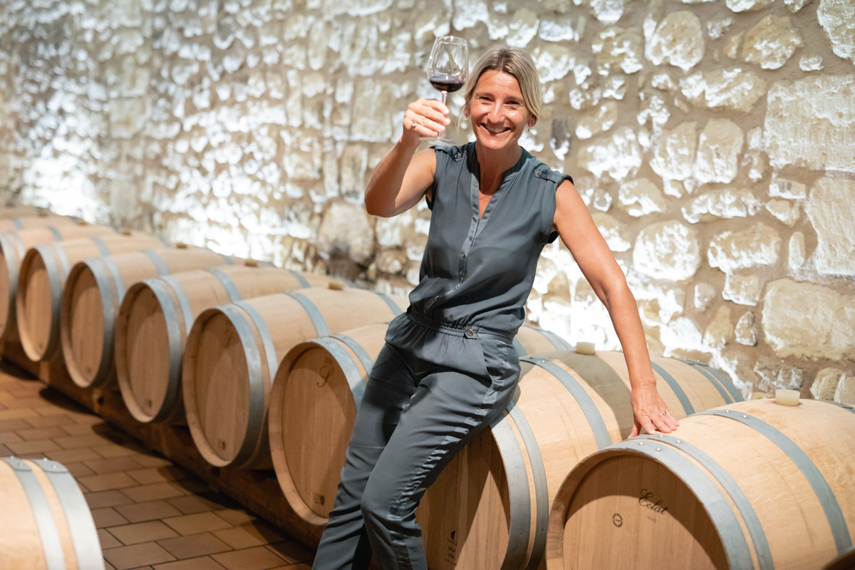 Brigitte Destouet raises a glass of her Le Veux Chateau Guibeau 1966 as she sits on a barrel in her winery's cellar
